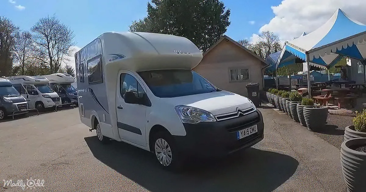A white Citroen camper van with a raised roof is parked in a sunny outdoor area with other campers and tents.