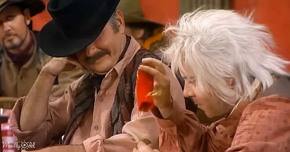 A man in a cowboy hat leans over another man with white hair, who is holding a bottle of red liquid.