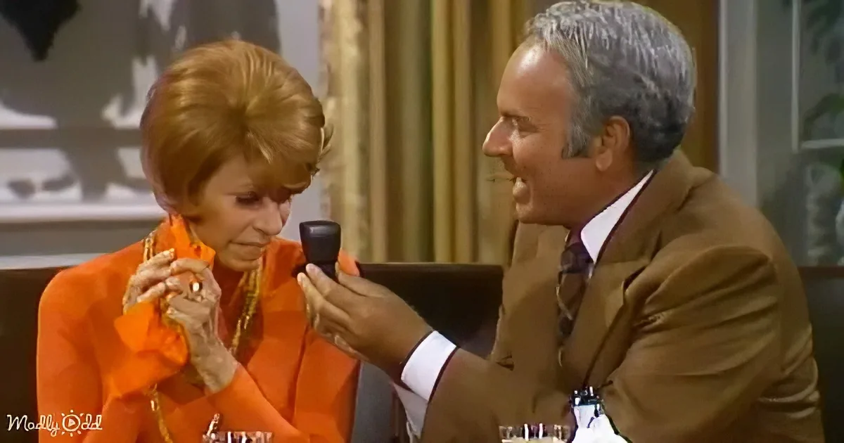 A man in a brown suit proposes to a woman in an orange dress with a ring.