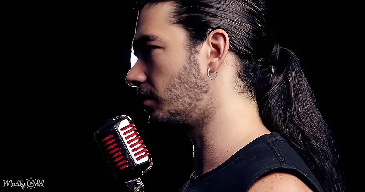 A man with long hair in a ponytail, wearing a black shirt, stands in profile with a vintage microphone.