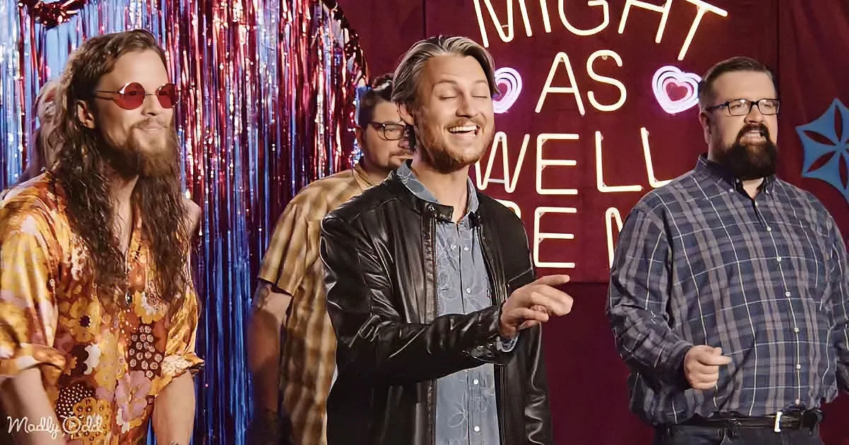 A man in a black leather jacket smiles while pointing, surrounded by others in a festive setting with a neon sign.