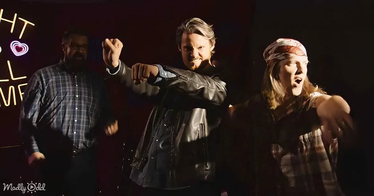 A man in a leather jacket raises his fist, flanked by two others, with a neon sign in the background.