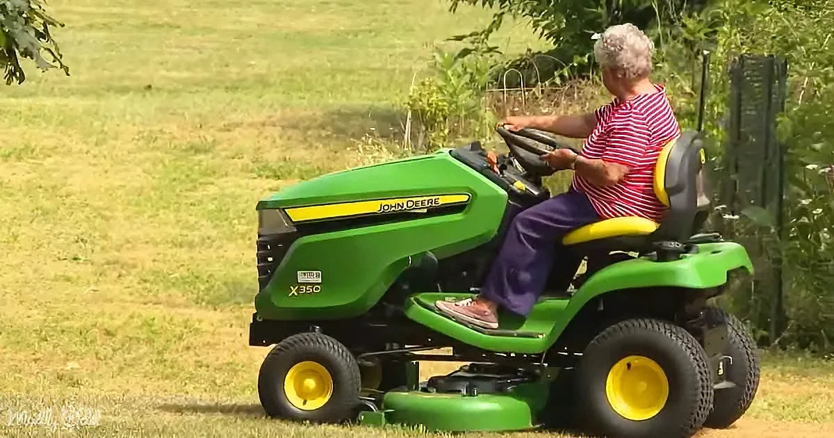 A person drives a green John Deere X350 riding lawn mower across a grassy field.