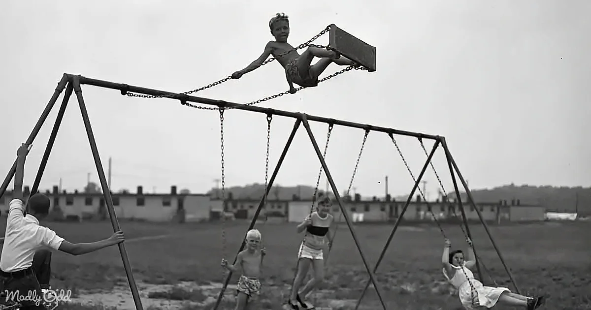 A boy swings high on a swing set while others play in the background.