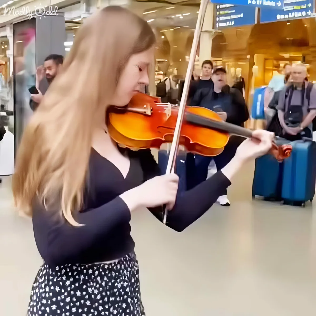 A woman with long blonde hair plays a violin in a busy airport terminal.