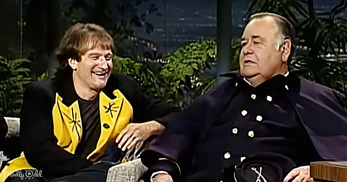 A man in a yellow and black jacket is laughing while sitting next to another man in a dark uniform.