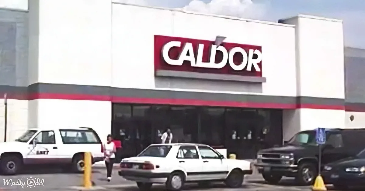 A Caldor store with a red and white sign, surrounded by parked cars and a person walking.