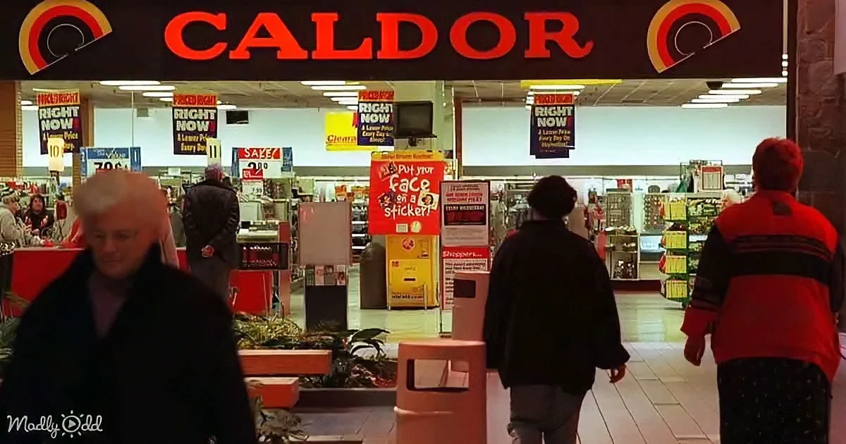 People walk inside a Caldor store with signs advertising "Right Now" deals and a "Put your face on a sticker" promotion.