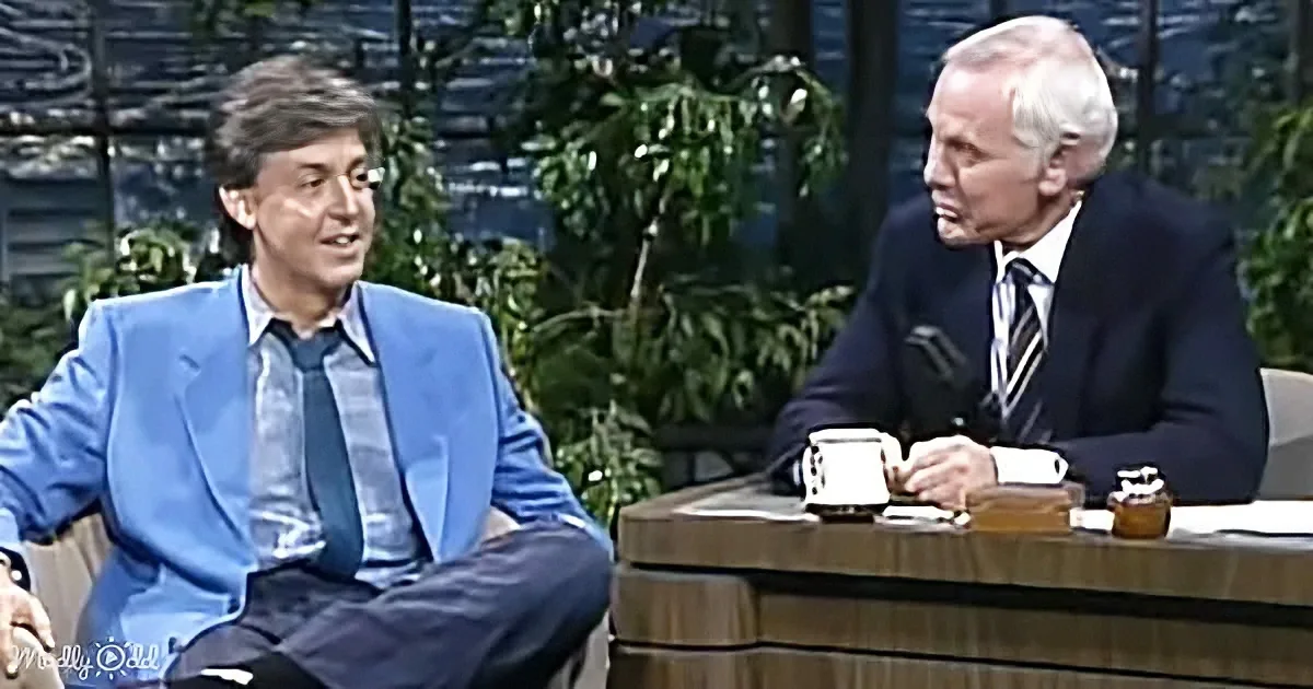 Paul McCartney in a blue suit sits on a talk show set, engaging with a host.