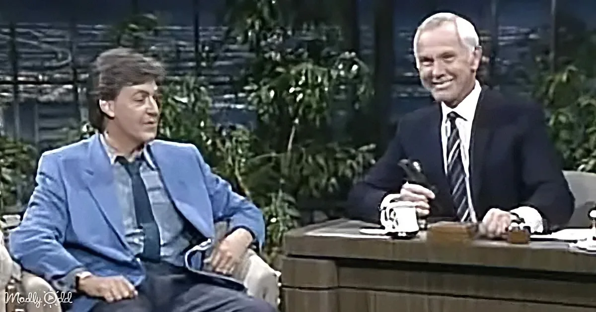 Steve Martin in a blue suit sits on a talk show set, engaging with a host in a dark suit.