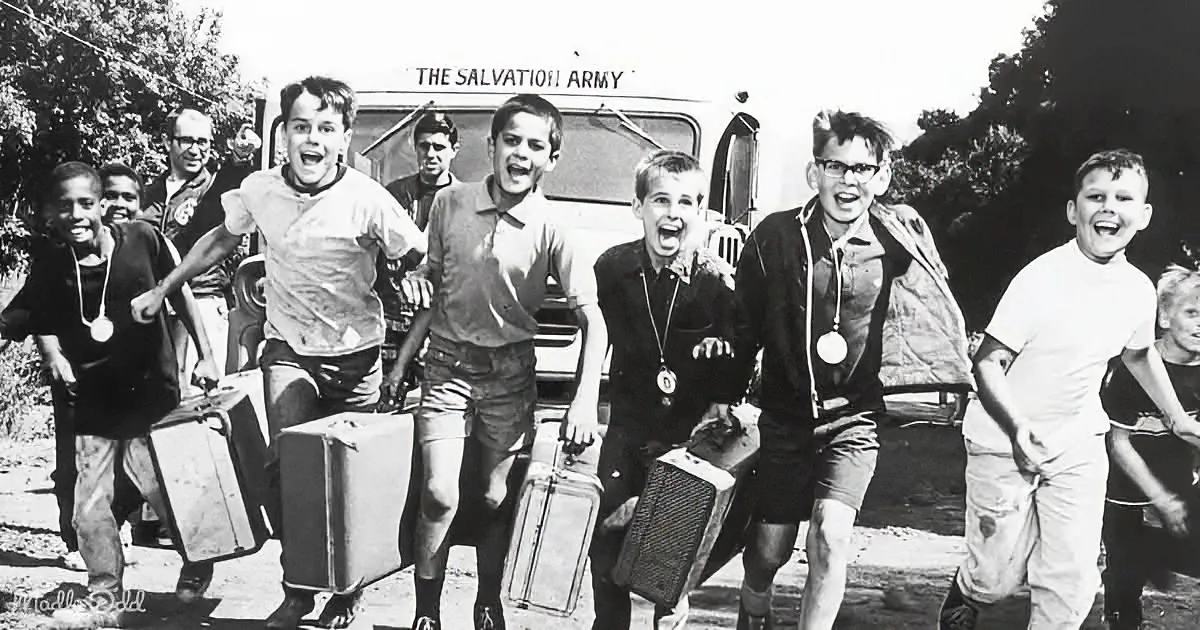 Children run joyfully with suitcases, laughing, in front of a Salvation Army van.