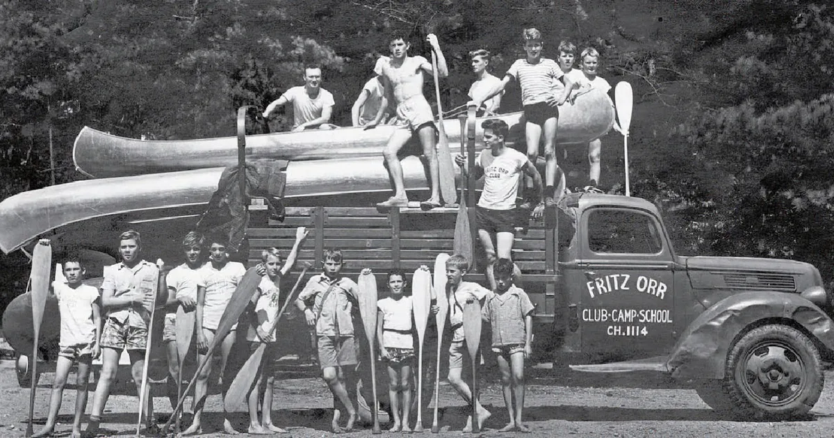 Teenagers with canoes and paddles pose on a vintage truck labeled "Fritz Orr Club-Camp-School."