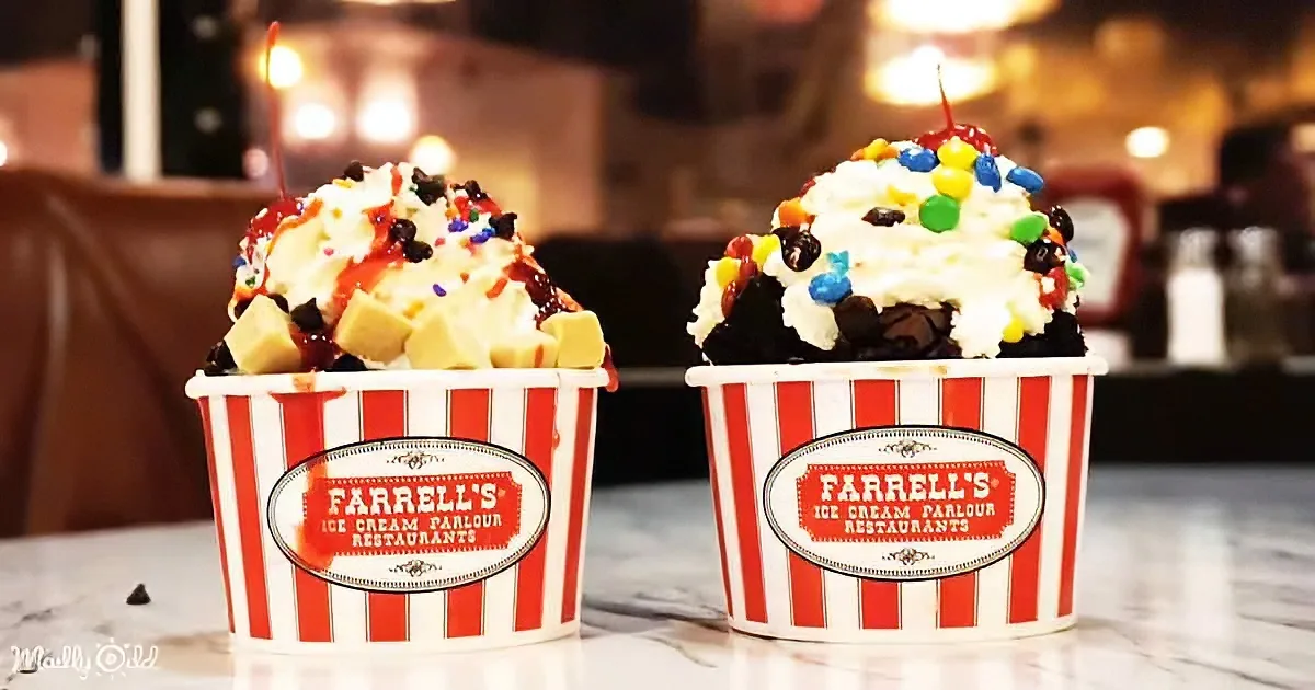 Two Farrell's ice cream sundaes with whipped cream, sprinkles, and a cherry on top sit in striped cups.