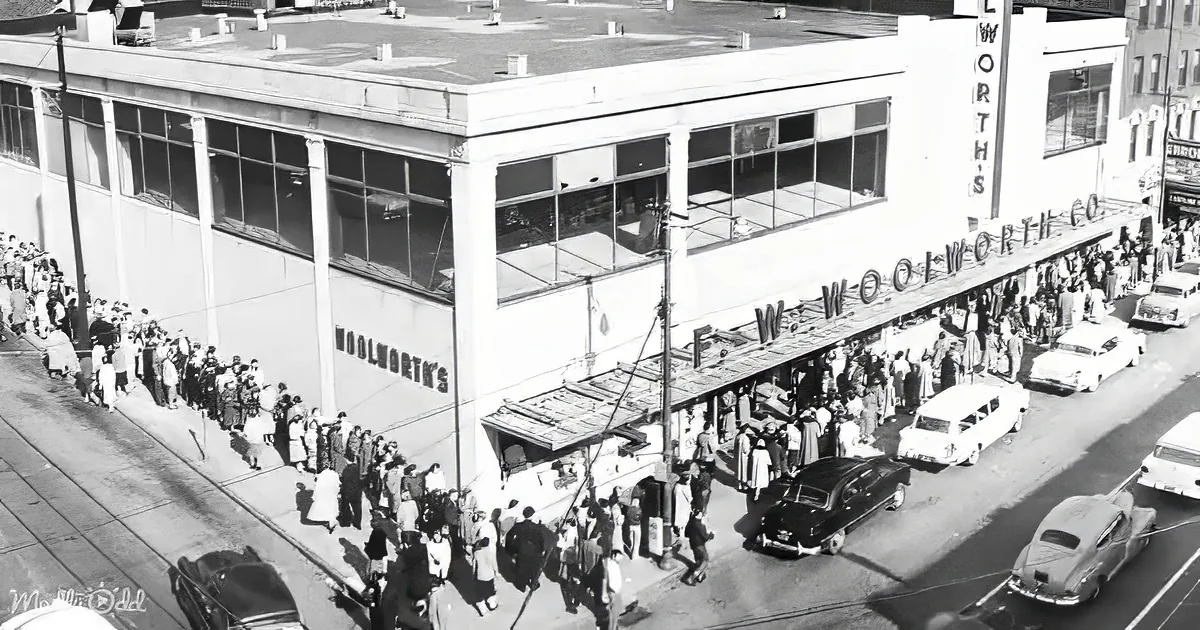 Crowds gather outside a Woolworth's store, with cars and a streetcar in the foreground.