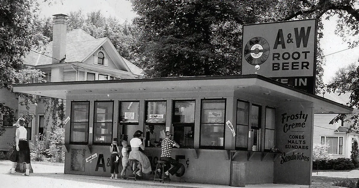 A group of people in white uniforms stands in front of an A&W Root Beer restaurant with a sign that says "Blink Your...