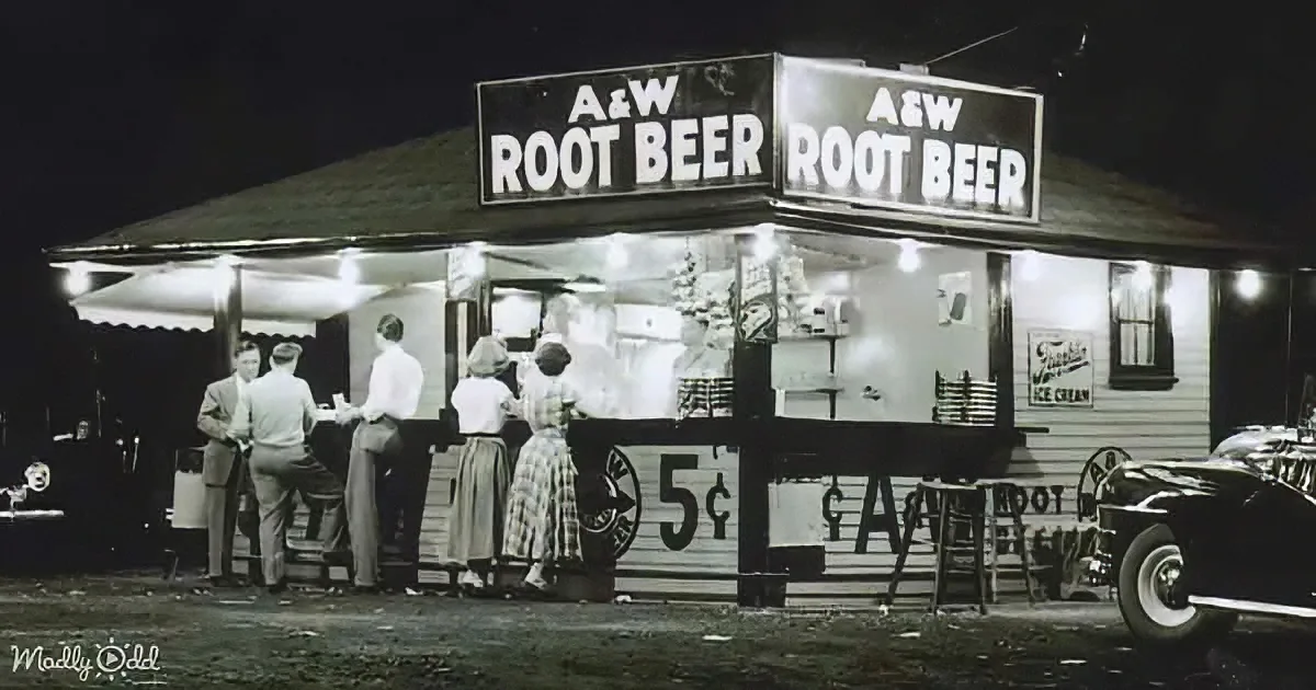 A&W Root Beer stand illuminated at night with people ordering, classic cars nearby.