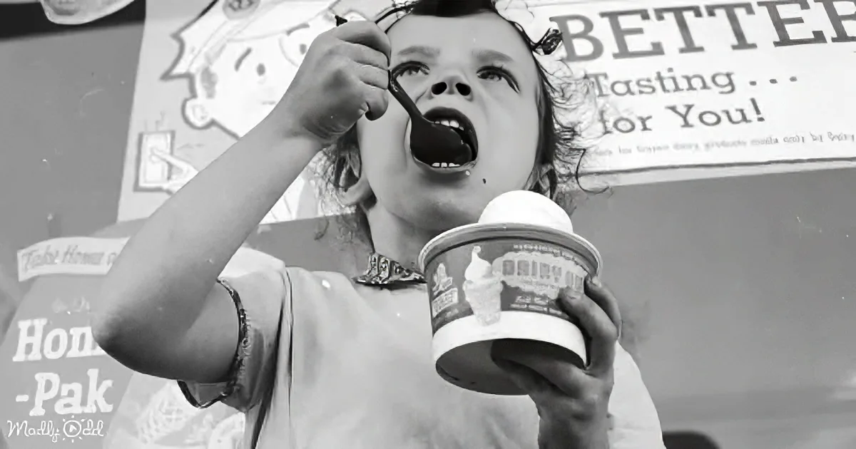 A child enjoys ice cream from a cup, spoon in hand, in front of a dairy advertisement.