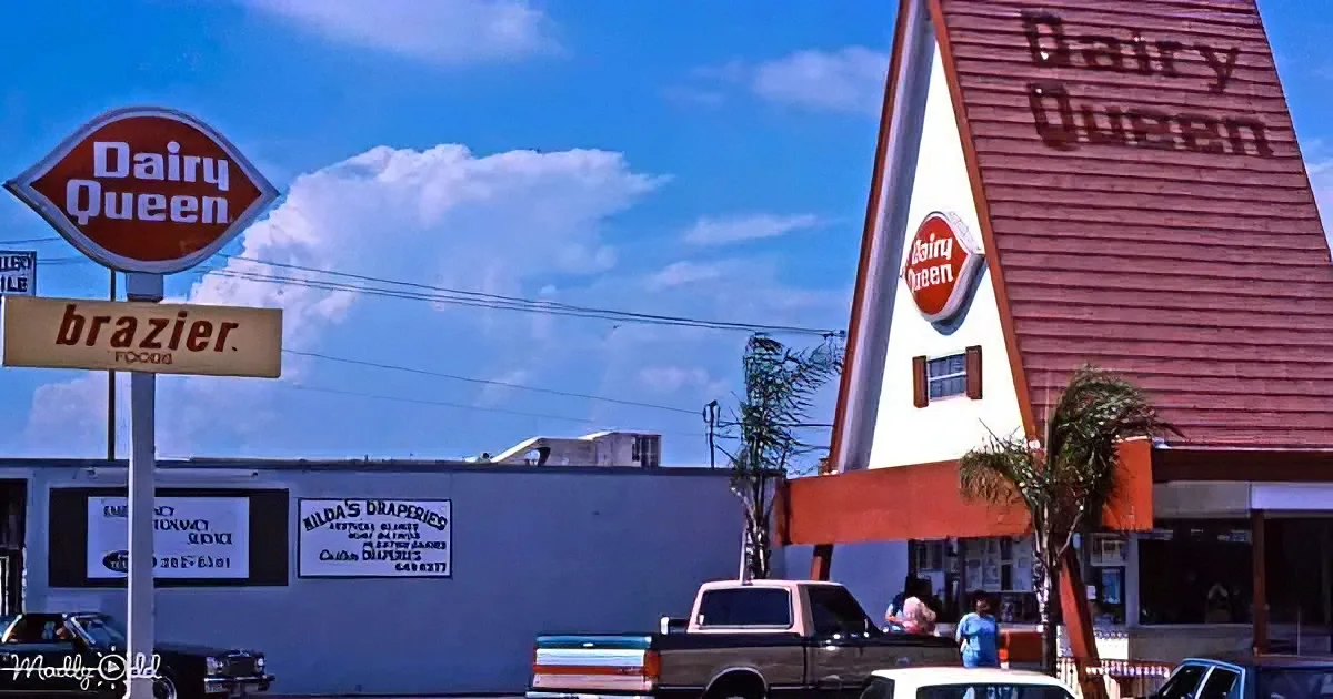 A Dairy Queen ice cream shop with a distinctive red and white triangular roof stands prominently against a blue sky.
