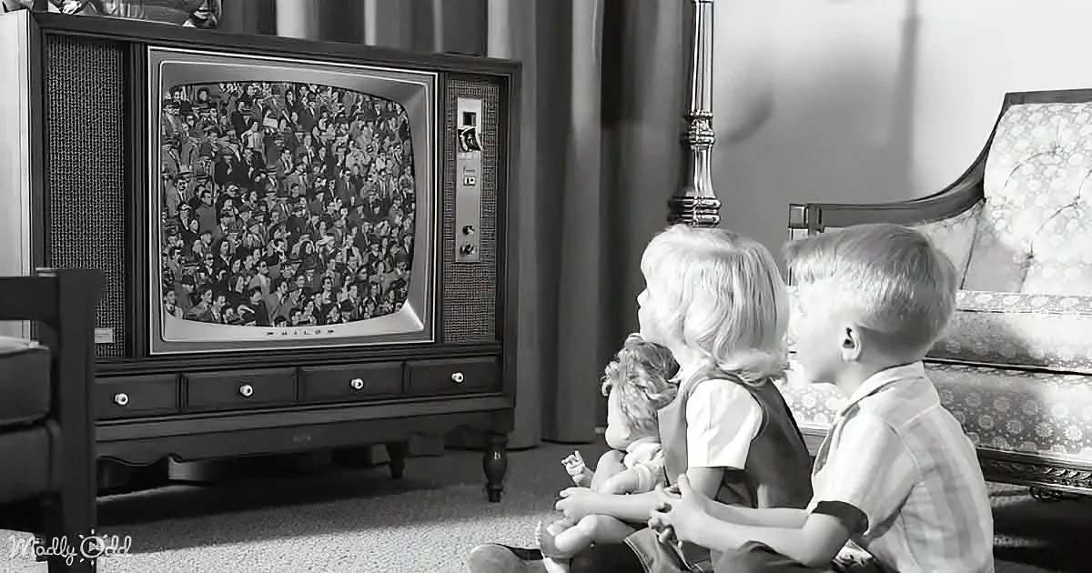 Three children sit on the floor watching an old television showing a crowd.