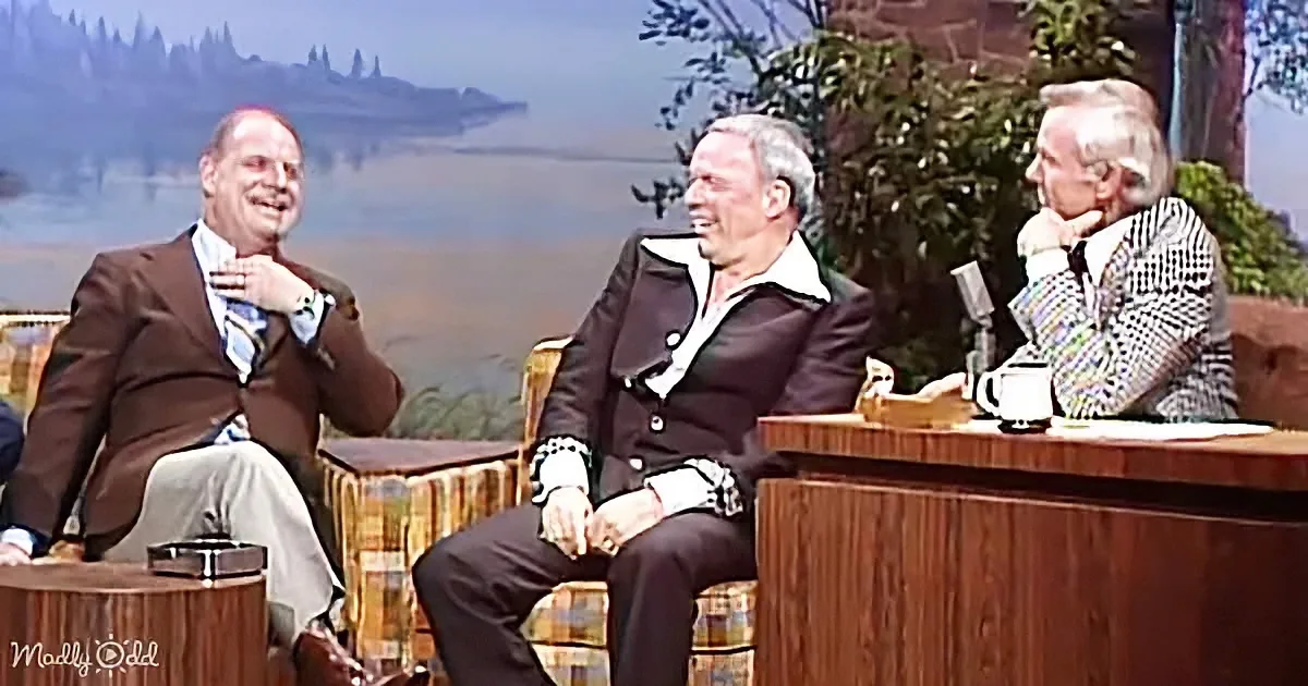Three men in suits sit on a talk show set, laughing and enjoying the conversation.