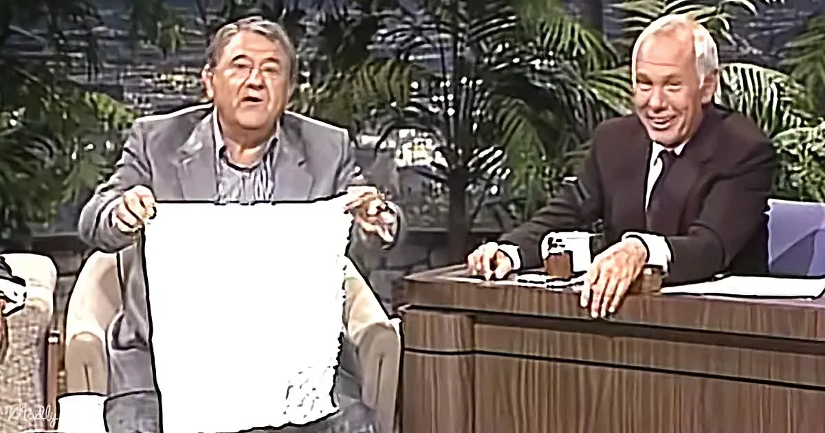A man holds a white sheet, appearing surprised, while another man sits at a desk, smiling.