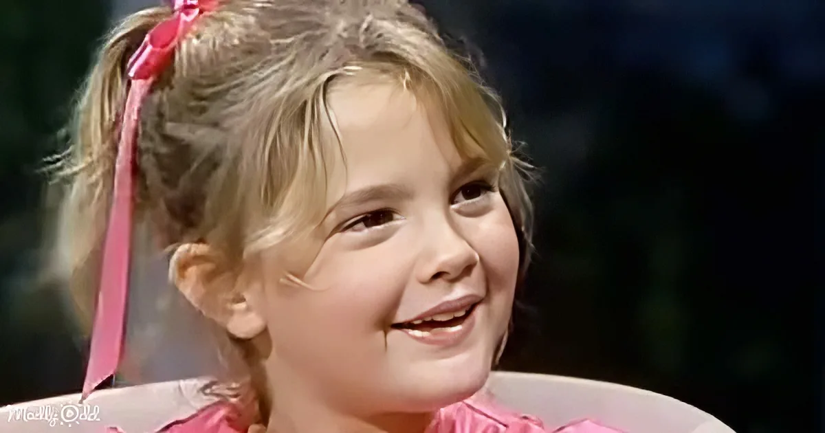 A young girl with blonde hair in pigtails, wearing a pink ribbon, smiles warmly.