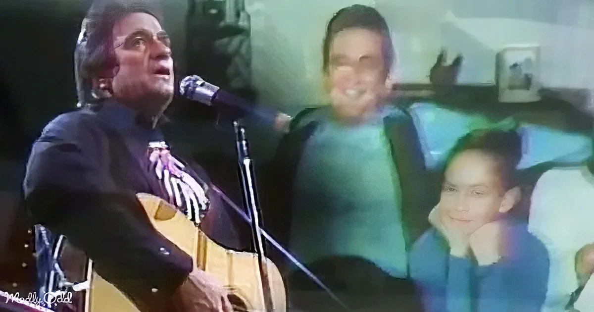 A man plays guitar and sings into a microphone while a smiling child sits behind him.