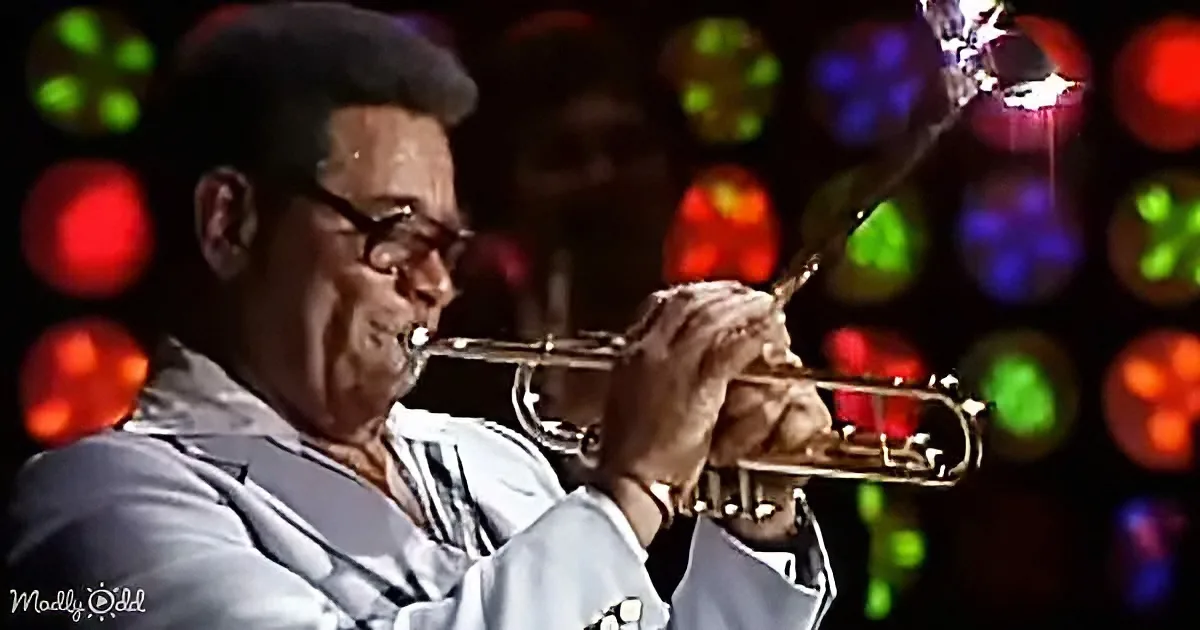 A man in a light blue suit plays a trumpet with colorful bokeh lights in the background.