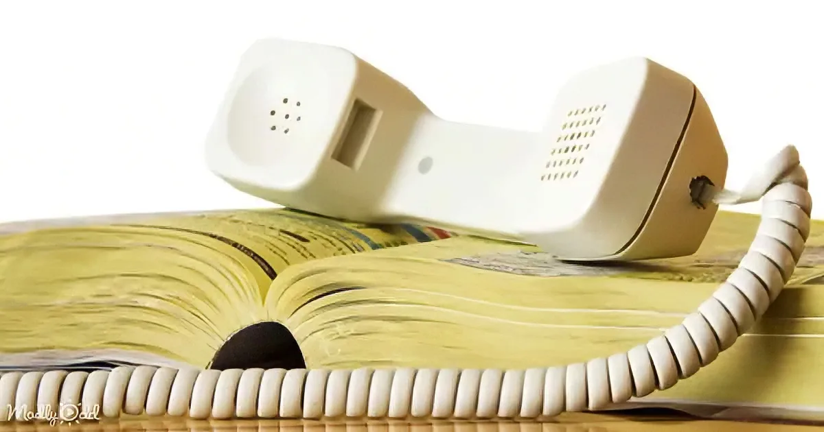 A vintage white telephone handset rests atop an open, yellowed book on a wooden surface.