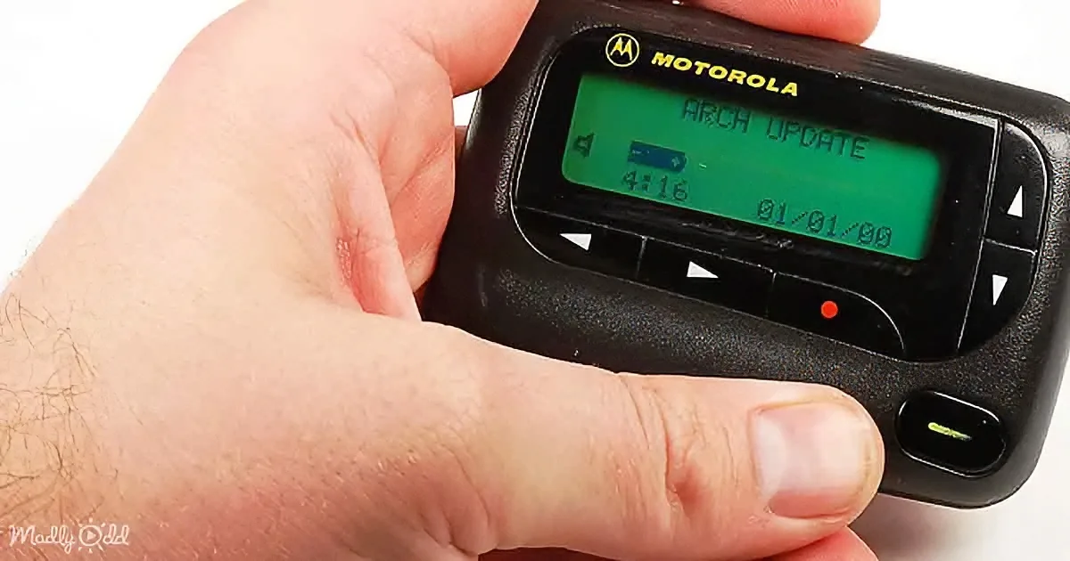 A hand holds a Motorola pager displaying "ARCH UPDATE" with a date and time.