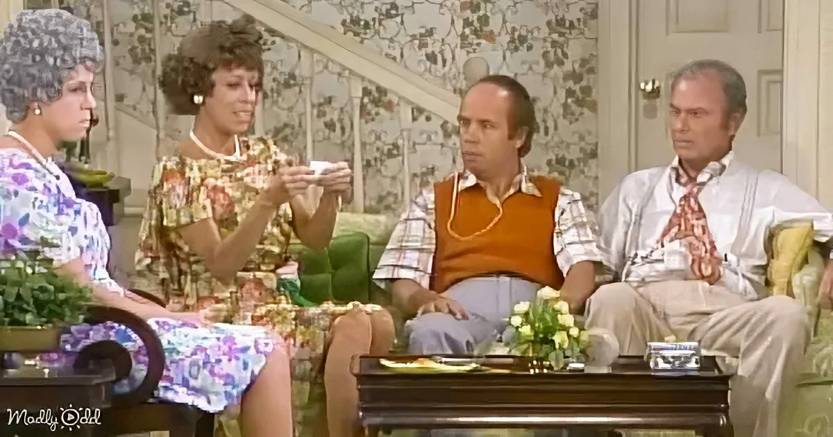 A woman in floral dress holds a tray, while four seated individuals in vintage attire engage in a conversation in a cozy...
