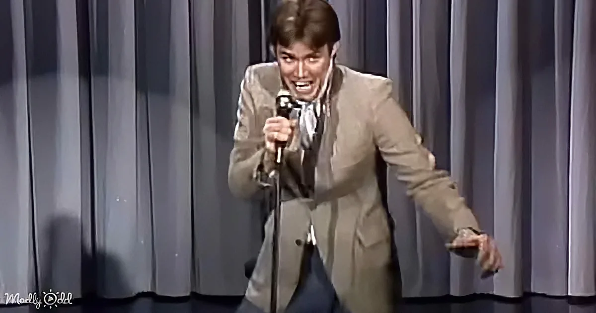 A man in a beige suit is passionately singing into a microphone on stage.