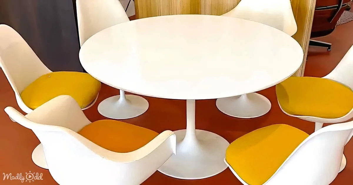 A modern white tulip table surrounded by white and yellow chairs on a red patterned floor.