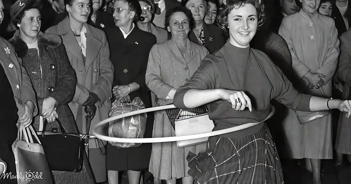 A woman smiles while holding a hula hoop, surrounded by a crowd of onlookers in a vintage setting.