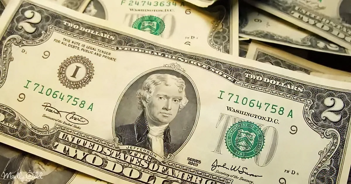 A two-dollar bill featuring Thomas Jefferson is prominently displayed amidst a pile of other dollar bills.