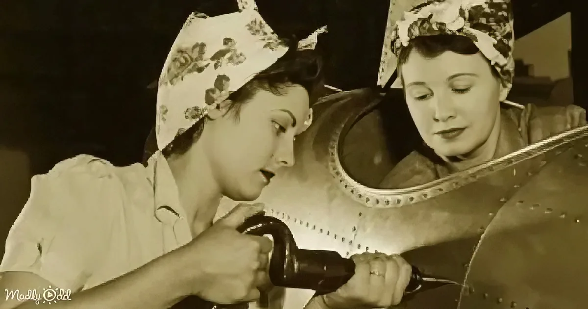 Two women in aprons work on a large metal object, possibly a wheel or part of a machine.