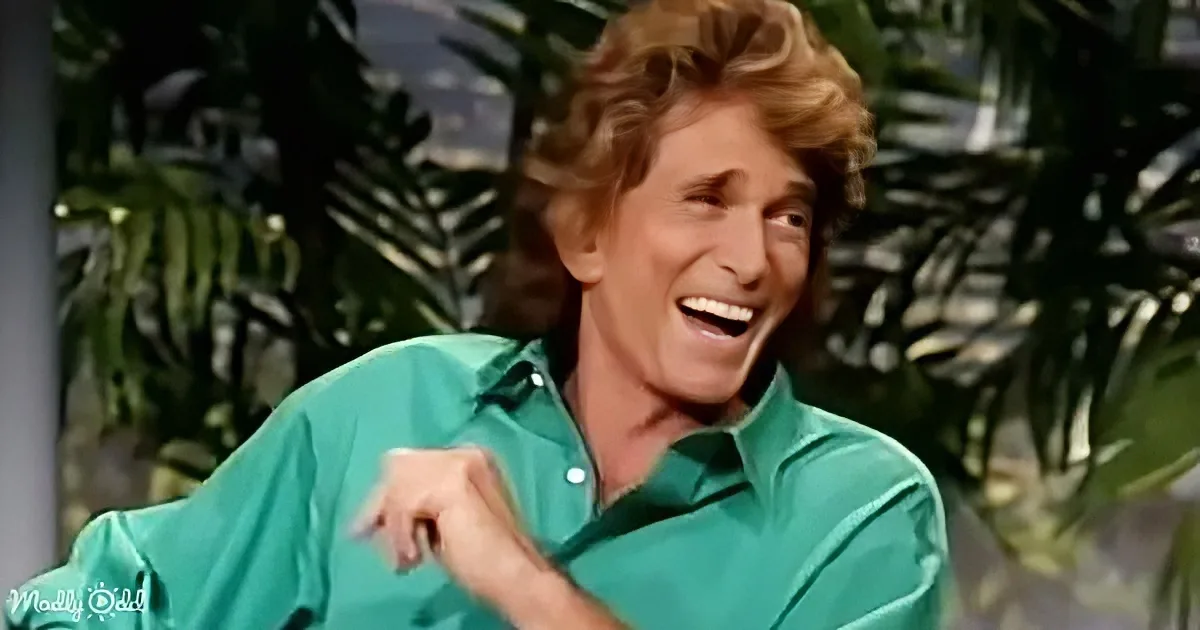 A person in a green shirt is smiling and gesturing with their hand, with palm trees in the background.