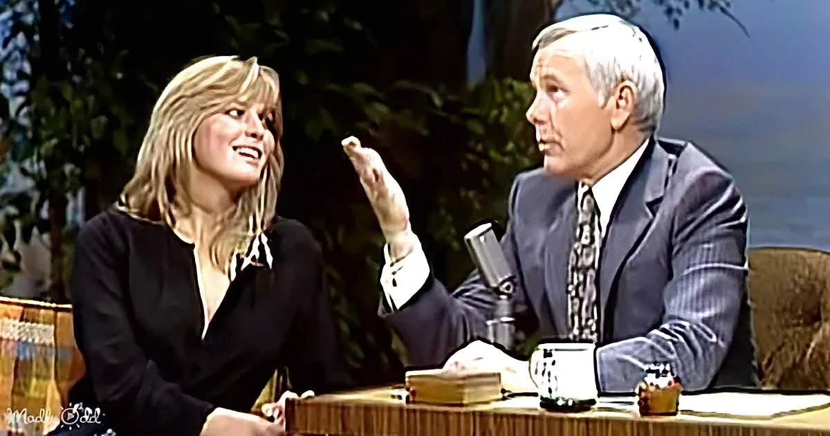 A woman in a black dress smiles while a man in a suit gestures during a talk show.