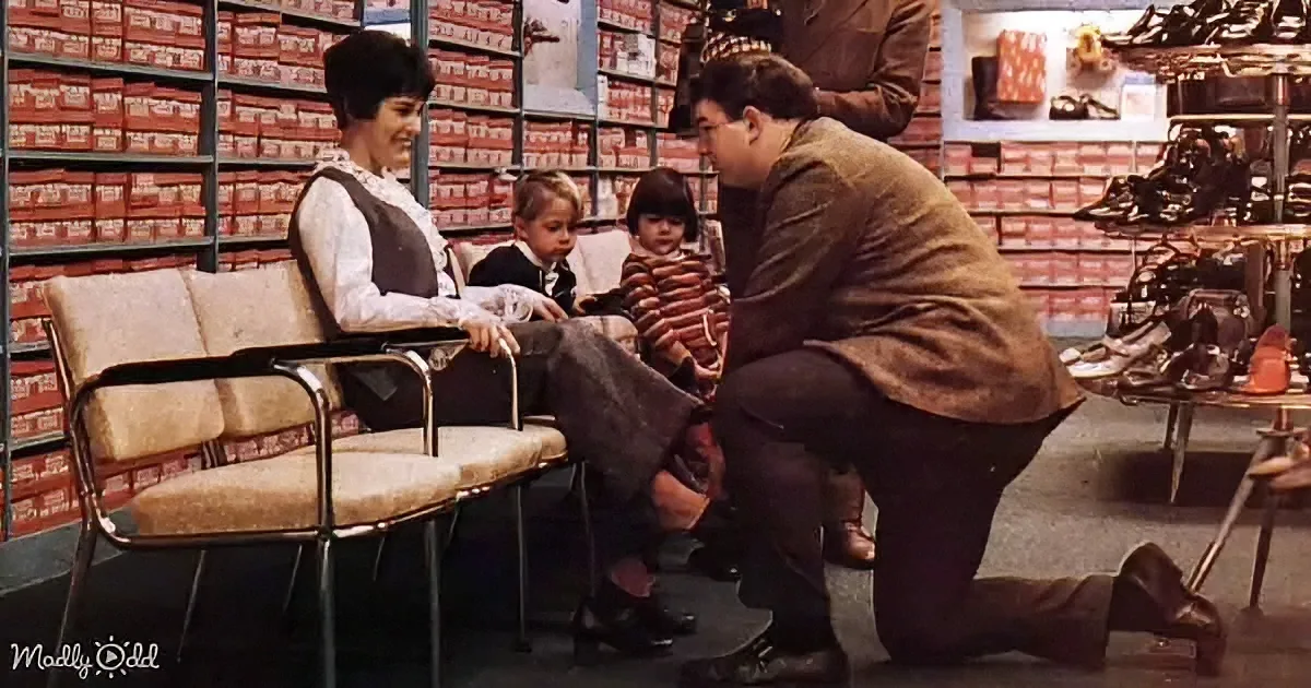 A man is trying on shoes in a shoe store, with a woman and two children watching.