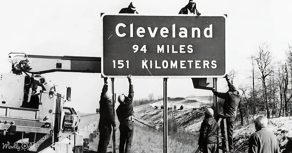 Workers install a sign indicating Cleveland is 94 miles/151 kilometers away.