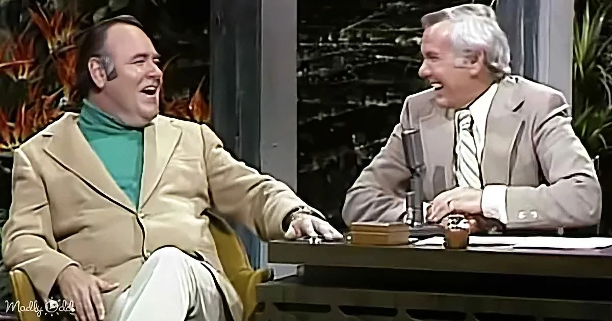 Two men in suits are laughing, one in a tan jacket and the other in a beige suit, seated at a desk.