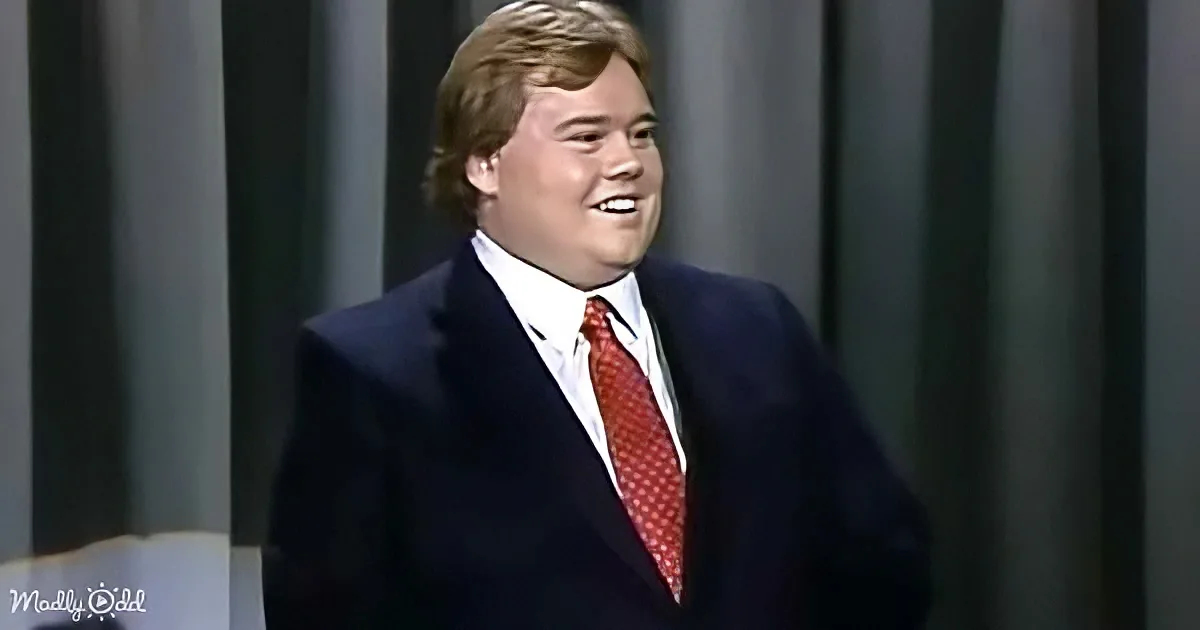 A man in a dark suit and red tie smiles, standing against a dark background.