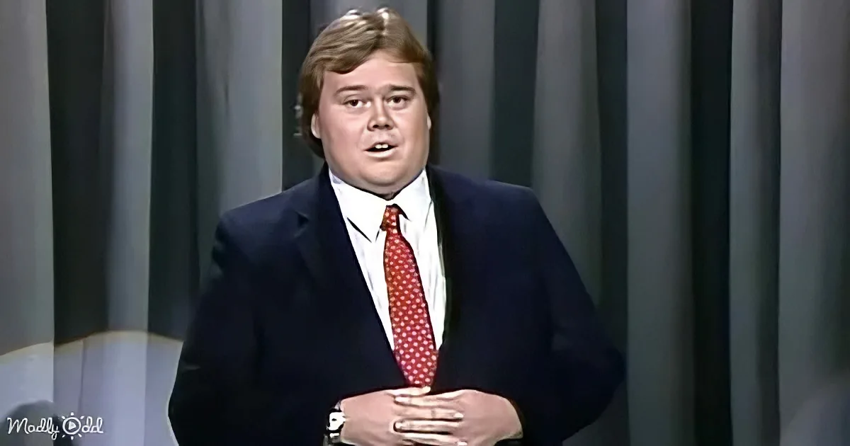 A man in a dark suit and red tie stands with hands clasped, looking slightly to the side.
