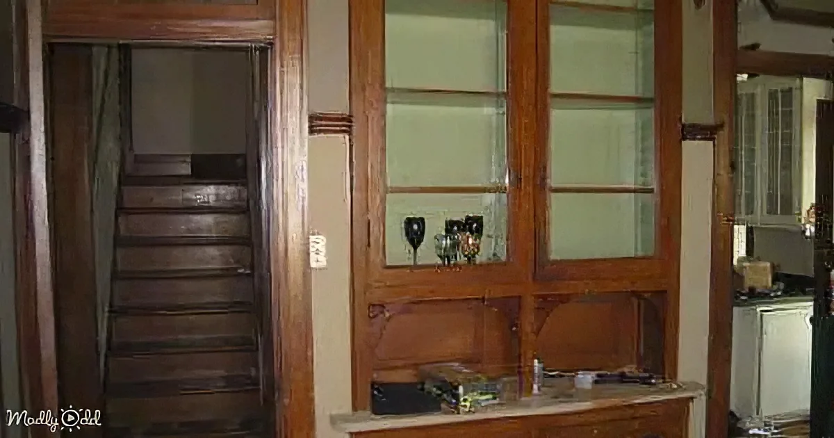 A wooden cabinet with glass doors and a staircase leading up to a door in the background.
