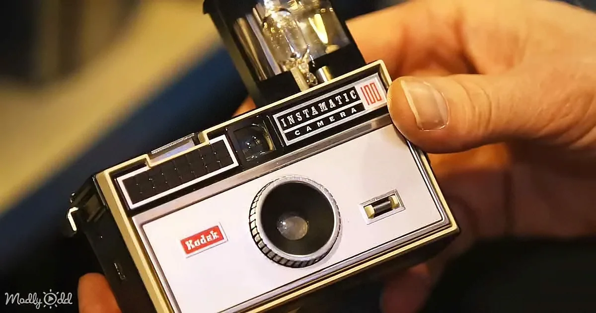 A Kodak Instamatic 100 camera is being held, showcasing its classic design and branding.