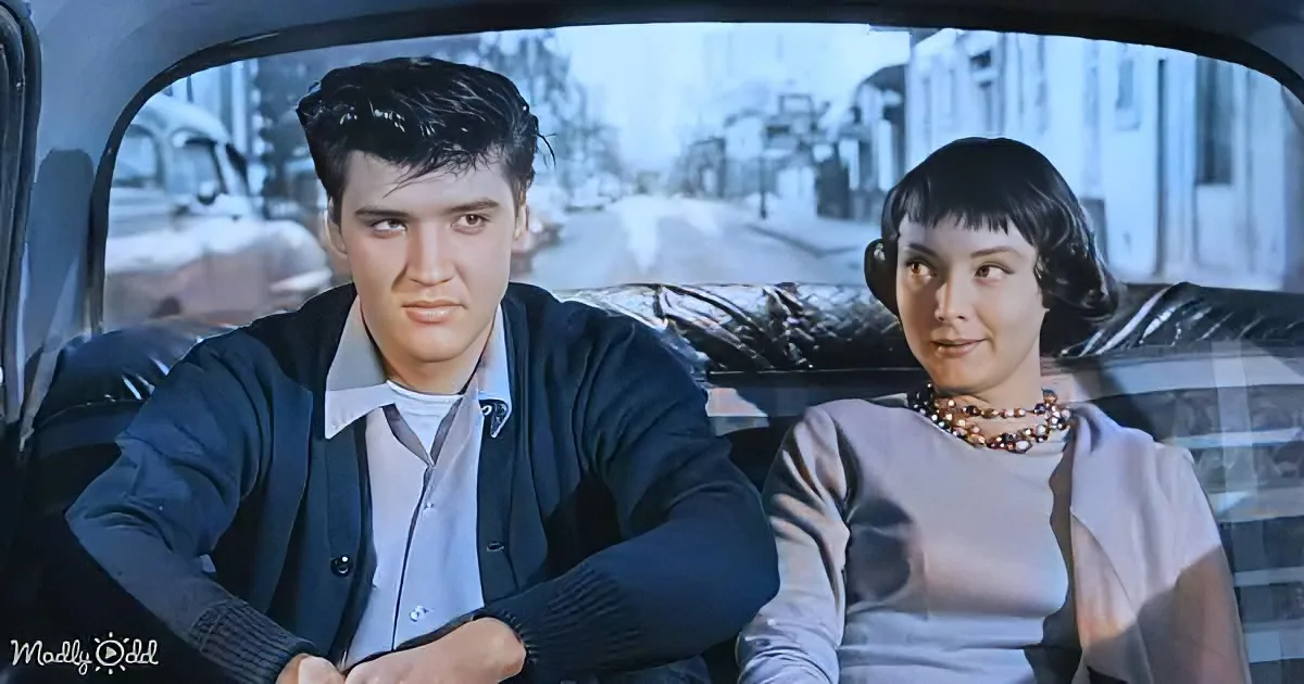 Elvis Presley and a woman sit in a car, looking ahead, with a snowy street in the background.