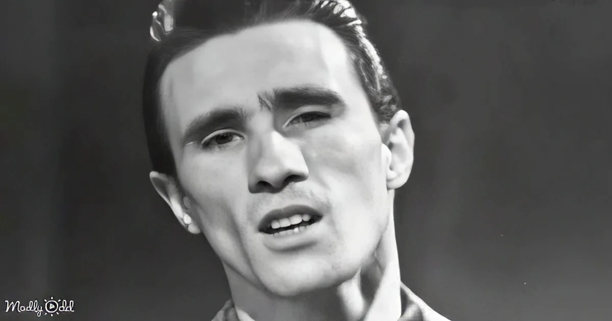 A man with slicked-back hair and a serious expression, wearing a collared shirt, is the main subject of this...