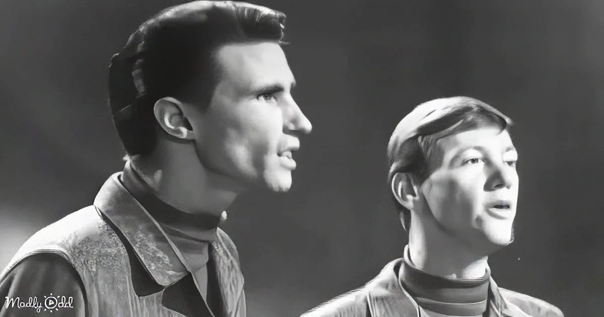 A man and a woman are singing, both wearing collared shirts, in a black-and-white image.