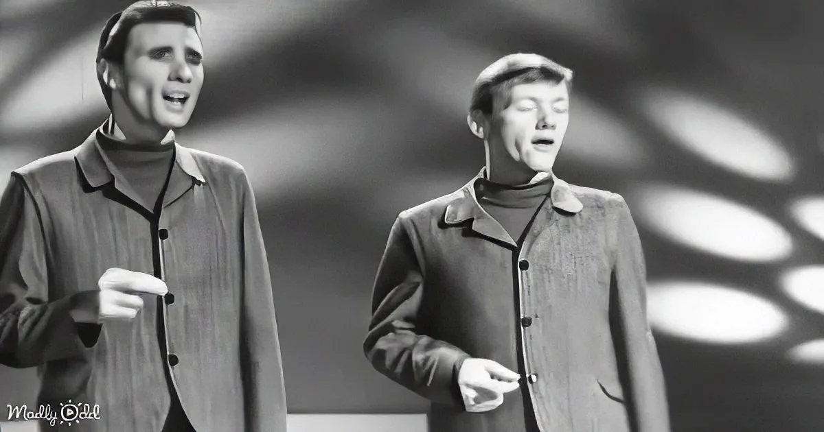 Two men in 1960s attire sing on stage, one pointing, both with expressive faces.