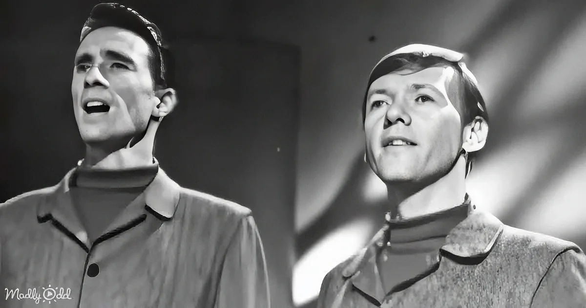 Two men in matching uniforms with high collars, one singing, both looking upwards.